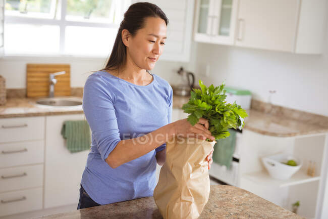 Feliz mulher asiática desembalar mantimentos frescos na cozinha. estilo de vida saudável e passar o tempo em casa. — Fotografia de Stock