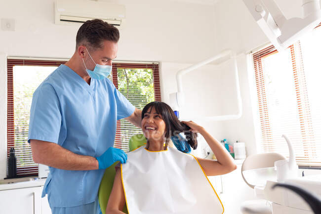 Dentista masculino caucasiano usando máscara facial preparando paciente do sexo feminino na clínica odontológica moderna. serviços de saúde e odontologia. — Fotografia de Stock