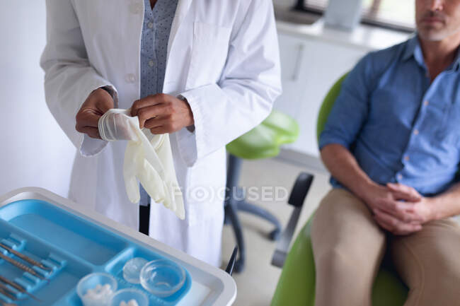 Двухсторонняя женщина-стоматолог в медицинских перчатках и пациент-мужчина, ожидающий в современной стоматологической клинике. здравоохранение и стоматология. — стоковое фото