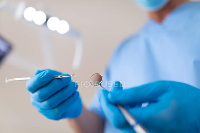 Dentista masculino caucásico usando mascarilla que sostiene herramientas dentales en la clínica dental moderna. negocio de salud y odontología. - foto de stock