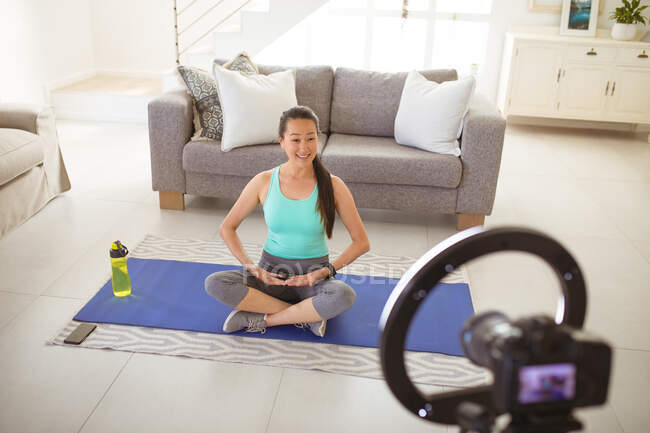 Щаслива азіатська жінка сидить на килимку, роблячи фітинги відеоблог з дому. здоровий активний спосіб життя і фізична підготовка вдома з технологіями . — стокове фото