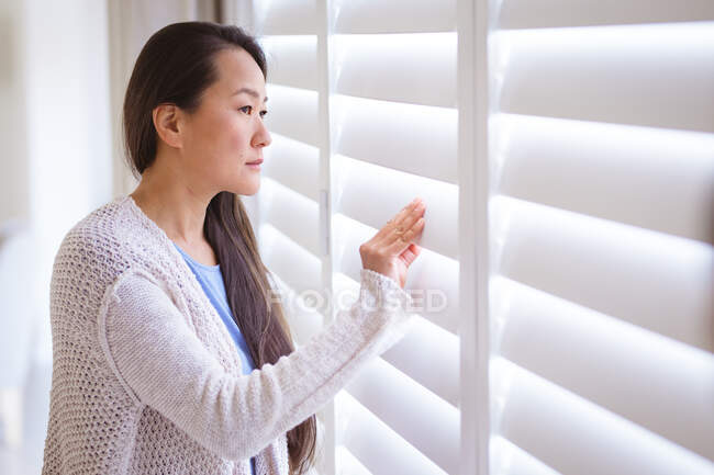 Profil de femme asiatique réfléchie debout à la fenêtre, regardant à l'extérieur. mode de vie, loisirs et passer du temps à la maison. — Photo de stock