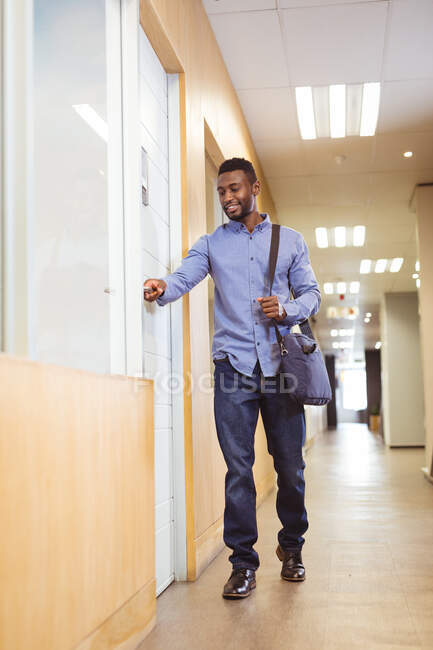 Empresário afro-americano sorridente andando e abrindo a porta no corredor no escritório moderno. empresa e escritório local de trabalho. — Fotografia de Stock