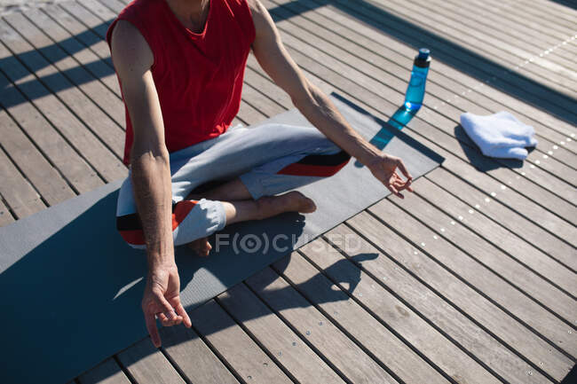 Low section of man sitting in lotus position meditating while praciticing yoga on floorboard. fitness and healthy lifestyle. — Stock Photo