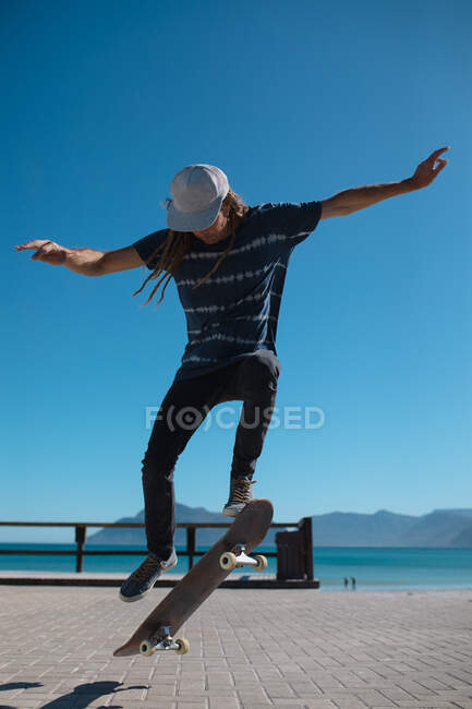 Männliche Skateboarder vollführen Stunt an der Promenade vor klarem blauem Himmel mit Kopierraum. Lifestyle und Sport. — Stockfoto
