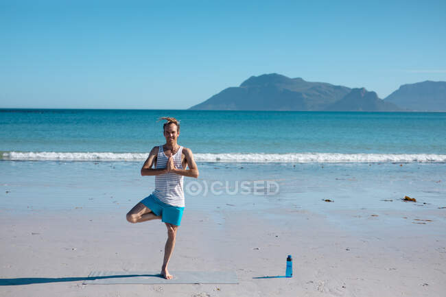 Чоловік, який практикує дерево, позує пози йоги на пляжі проти прозорого блакитного неба з копіювальним простором. фітнес і здоровий спосіб життя . — стокове фото