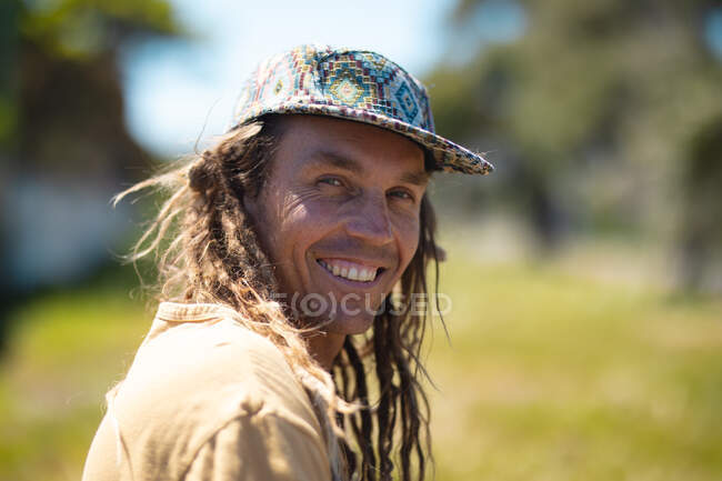 Retrato de un pintor de murales hipster masculino sonriente con gorra mirando por encima del hombro en un día soleado. hipster personas. - foto de stock
