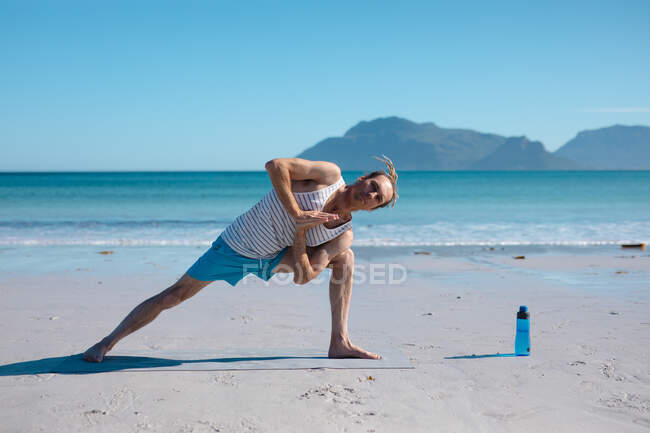Piena lunghezza di uomo flessibile praticare yoga posa in spiaggia contro cielo blu chiaro con spazio copia. fitness e stile di vita sano. — Foto stock