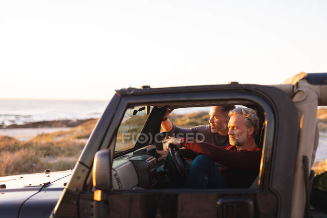 Heureux couple gay caucasien assis en voiture au bord de la mer. road trip d'été et vacances dans la nature. — Photo de stock