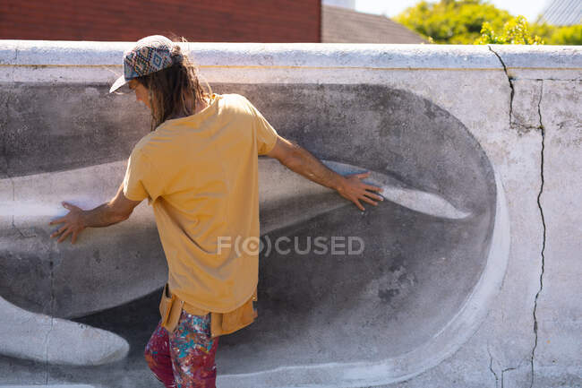 Задний вид мужчины-художника, идущего, прикасаясь к фреске кита на стене. стрит-арт и мастерство. — стоковое фото