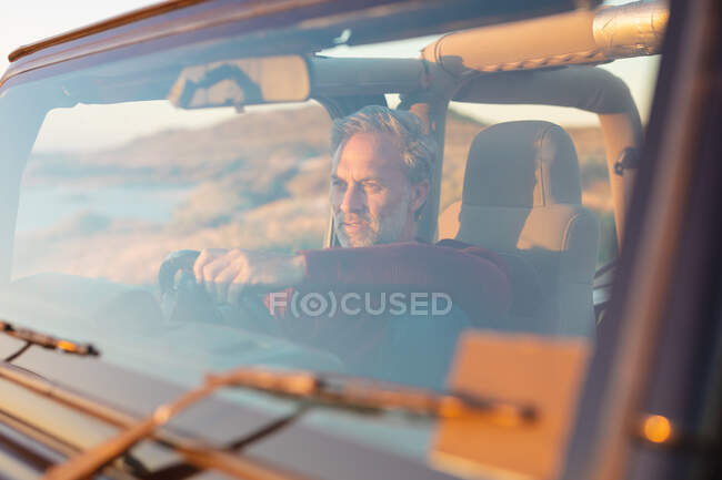 Pensativo hombre caucásico sentado en el coche a la orilla del mar admirando la vista. viaje por carretera de verano y vacaciones en la naturaleza. - foto de stock