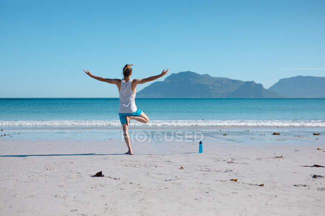 Visão traseira do homem praticando pose de árvore com os braços estendidos na praia em frente ao espaço de cópia. fitness e estilo de vida saudável. — Fotografia de Stock