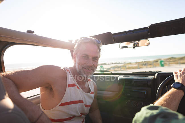 Porträt eines lächelnden kaukasischen Mannes, der mit einem Freund an einem sonnigen Tag am Meer im Auto sitzt. Sommer Roadtrip und Urlaub in der Natur. — Stockfoto