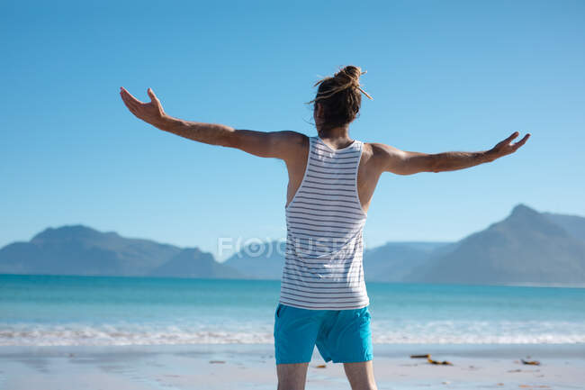 Задний вид человека, стоящего с распростертыми руками, смотрящего в сторону моря на фоне голубого неба. отдых и природа. — стоковое фото