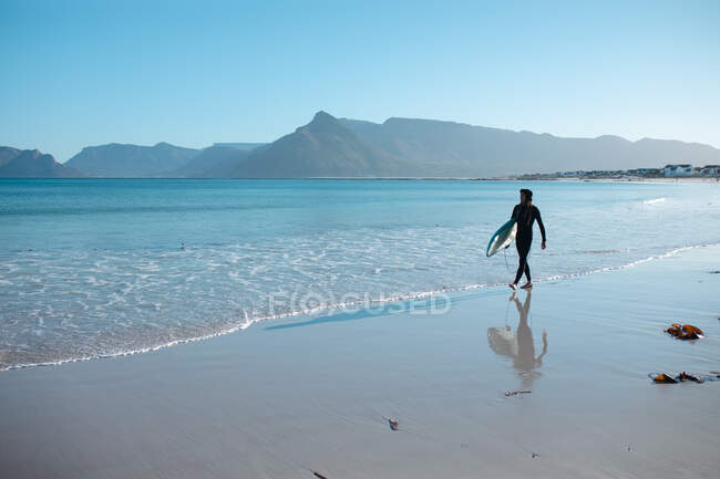 Surfeur masculin marchant le long de la rive avec planche de surf contre ciel bleu clair et l'espace de copie. hobbies et sports nautiques. — Photo de stock