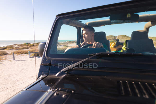 Thoughtful caucasian man sitting in car on sunny day at seaside. summer road trip and holiday in nature. — Stock Photo