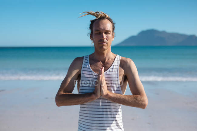 Хипстерский человек с сжатыми руками и закрытыми глазами медитирует во время занятий йогой на пляже. фитнес и здоровый образ жизни. — стоковое фото