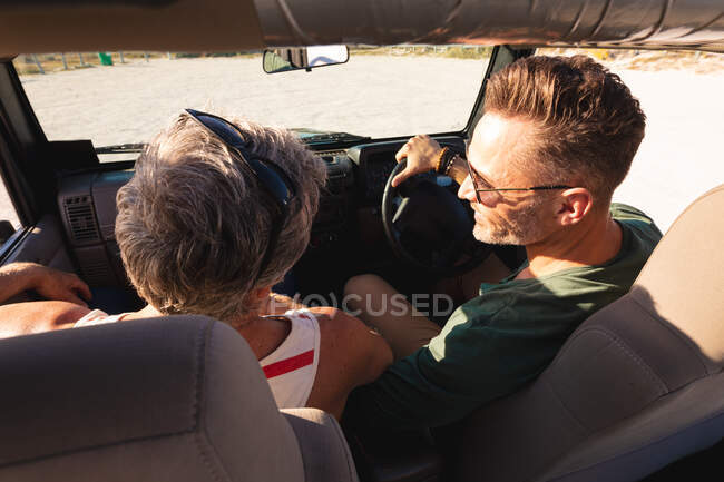 Heureux couple gay caucasien assis en voiture le jour ensoleillé au bord de la mer. road trip d'été et vacances dans la nature. — Photo de stock