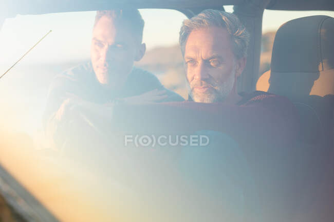 Happy caucasian gay male couple sitting in car at seaside admiring the view. summer road trip and holiday in nature. — Stock Photo