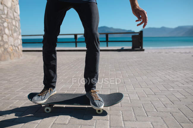 Baixa seção de skate homem no passeio marítimo contra o céu durante o dia ensolarado. estilo de vida e desporto. — Fotografia de Stock