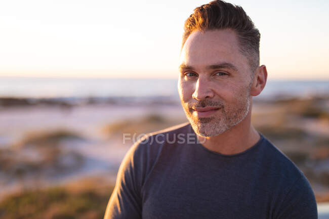 Retrato de un hombre caucásico sonriente mirando la cámara en la playa junto al mar. viaje por carretera de verano y vacaciones en la naturaleza. - foto de stock