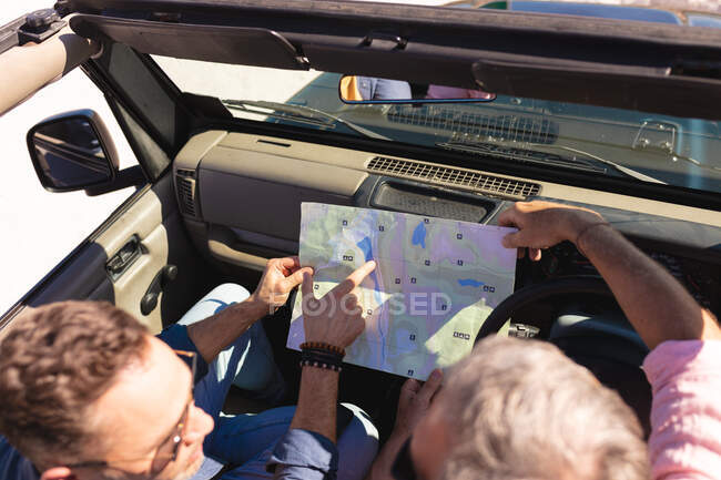 Caucasian gay male couple reading map sitting in car at seaside. summer road trip and holiday in nature. — Stock Photo