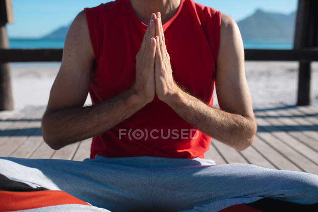 Der Mittelteil des Mannes mit den Händen umklammerte sich beim Meditieren, während er an sonnigen Tagen Yoga am Strand praktizierte. Fitness und gesunder Lebensstil. — Stockfoto