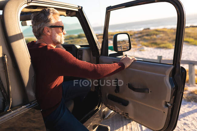 Щасливий білий чоловік в сонцезахисних окулярах відкриває двері автомобіля на узбережжі в сонячний день. літня дорога поїздка і відпочинок на природі . — стокове фото