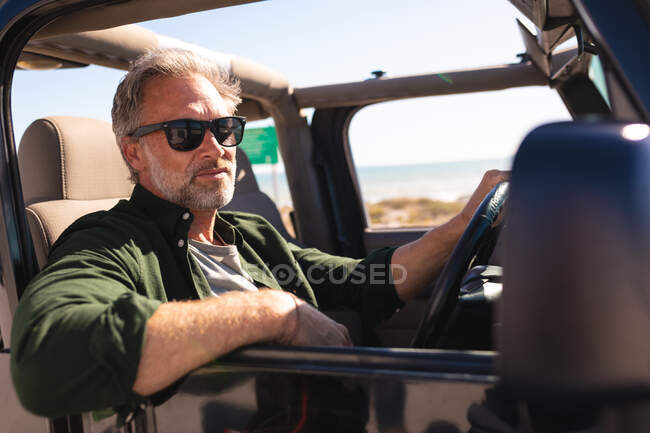 Retrato de homem caucasiano em óculos de sol sentado no carro à beira-mar. viagem de verão e férias na natureza. — Fotografia de Stock
