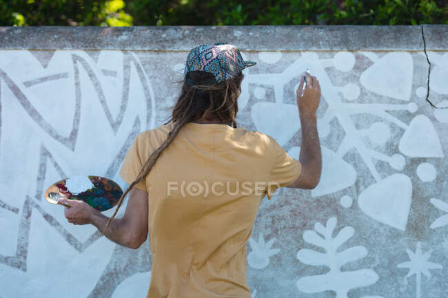Visão traseira do artista masculino segurando paleta enquanto pintura mural abstrato na parede. arte de rua e habilidade. — Fotografia de Stock