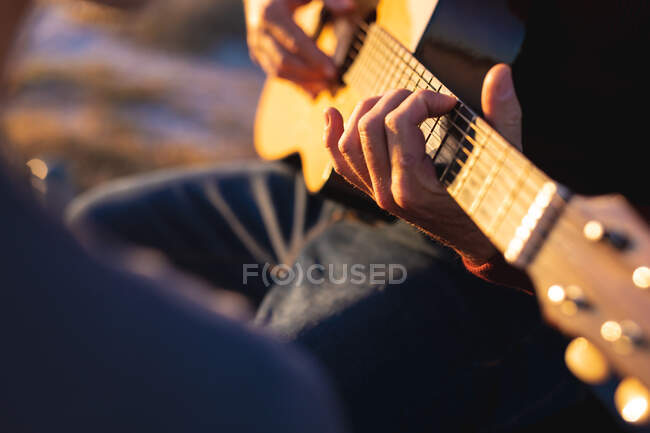 Sección media del hombre tocando la guitarra en la playa al atardecer. viaje por carretera de verano y vacaciones en la naturaleza. - foto de stock