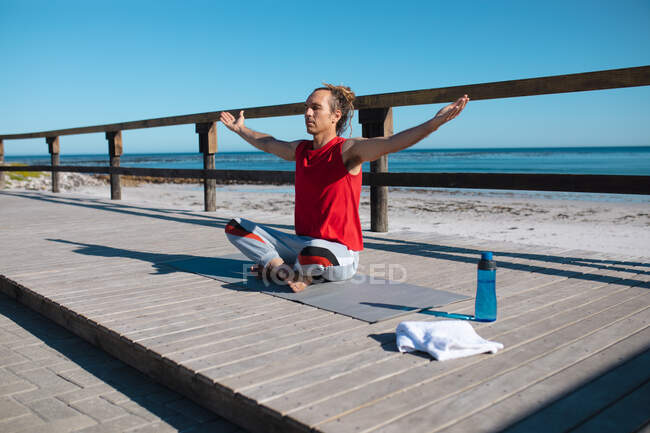 Mann sitzt im Schneidersitz mit ausgestreckten Armen und meditiert, während er Yoga auf Dielenbrett praktiziert. Fitness und gesunder Lebensstil. — Stockfoto