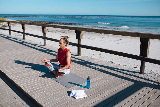 Man meditating while practicing yoga on floorboard at beach during sunny day. fitness and healthy lifestyle. — Stock Photo