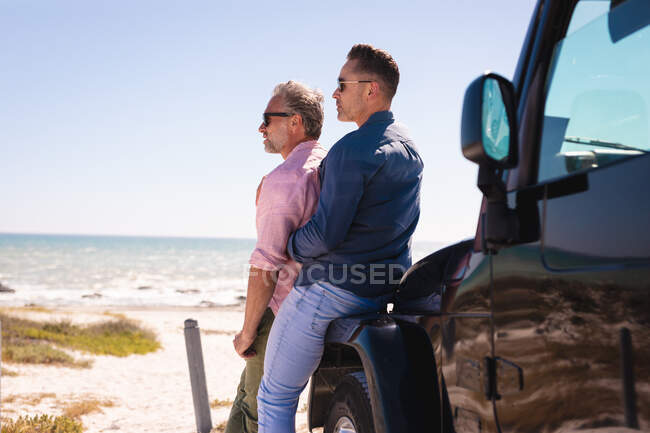 Glückliche kaukasische schwule männliche Paar umarmen und genießen die Aussicht mit dem Auto am Meer. Sommer Roadtrip und Urlaub in der Natur. — Stockfoto