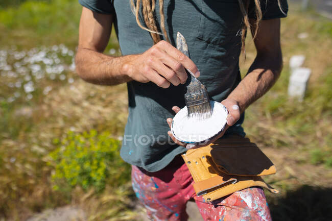 Midsection of male mural artist mixing paint with paintbrush during sunny day. skill and creativity. — Stock Photo