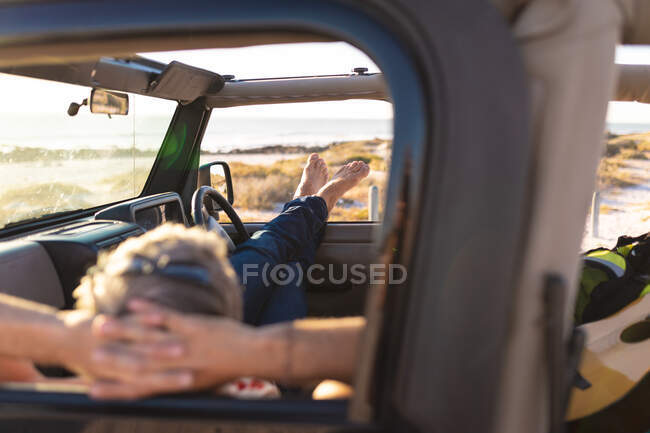 Homme caucasien détendu allongé en voiture, reposant au bord de la mer. road trip d'été et vacances dans la nature. — Photo de stock