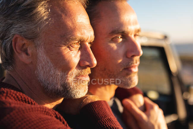 Feliz pareja gay caucásica abrazándose en el sol, disfrutando de la vista al mar. viaje por carretera de verano y vacaciones en la naturaleza. - foto de stock
