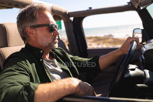Homme caucasien réfléchi dans des lunettes de soleil assis en voiture au bord de la mer. road trip d'été et vacances dans la nature. — Photo de stock