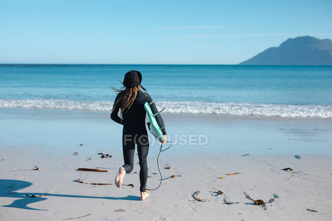 Vista trasera del surfista masculino corriendo con tabla de surf en la orilla hacia el mar durante el día soleado. pasatiempos y deportes acuáticos. - foto de stock