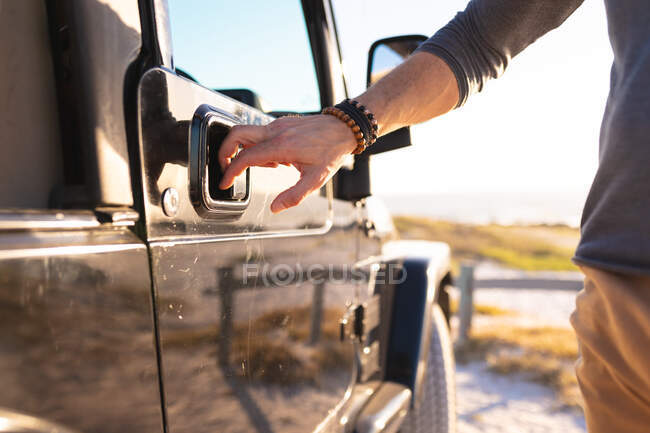 Midsection of man opening car door on beach by the sea. summer road trip and holiday in nature. — Stock Photo