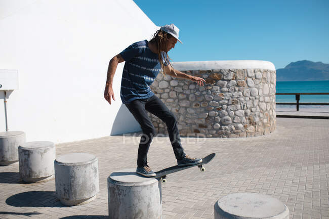 Полная длина скейтбордиста мужского пола, балансирующего на бетонной балладе на набережной в солнечный день. образ жизни и спорт. — стоковое фото