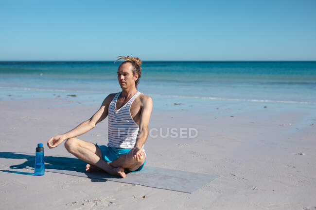 Mann sitzt im Schneidersitz und praktiziert Lotus-Positions-Yoga, während er mit Kopierraum gegen den Himmel meditiert. Fitness und gesunder Lebensstil. — Stockfoto