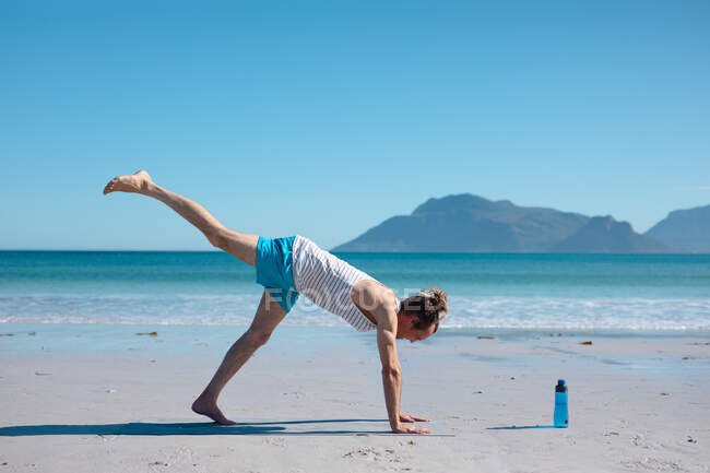 Hipster man practicing downward dog pose yoga with one leg up against blue sky and copy space. fitness and healthy lifestyle. — Stock Photo