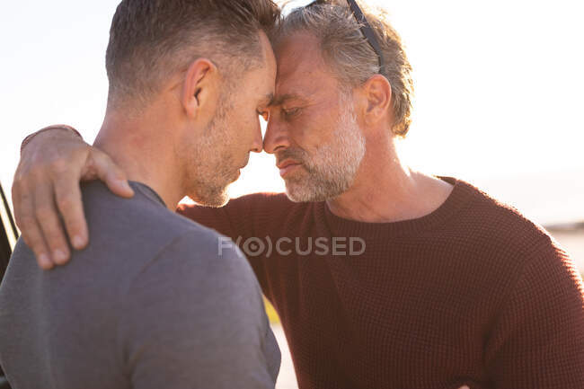 Feliz pareja gay caucásica abrazándose al sol en la playa. viaje por carretera de verano y vacaciones en la naturaleza. - foto de stock