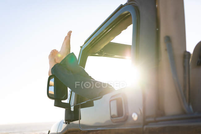Mann ruht sich im Auto aus, streckt die Beine aus dem Fenster, an einem sonnigen Tag am Meer. Sommer Roadtrip und Urlaub in der Natur. — Stockfoto