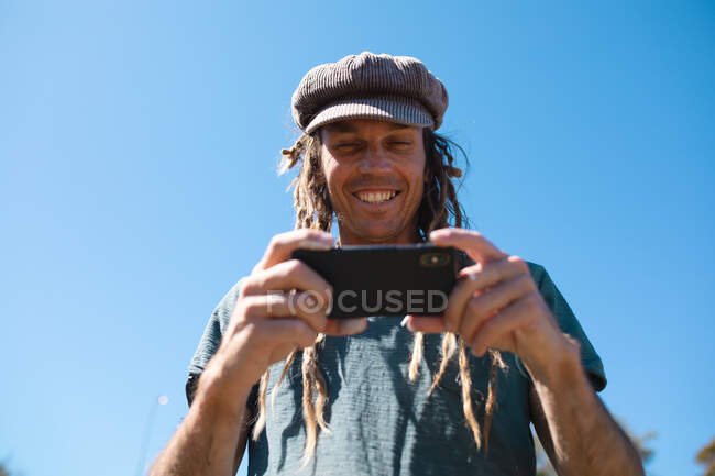Artista hipster maschio sorridente utilizzando smartphone contro cielo blu chiaro con spazio copia. tecnologia e hipster persone. — Foto stock