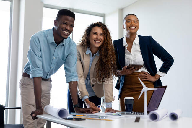 Alegres colegas de negocios multirraciales masculinos y femeninos en el escritorio en la oficina creativa. negocio, arquitecto y oficina creativa. - foto de stock