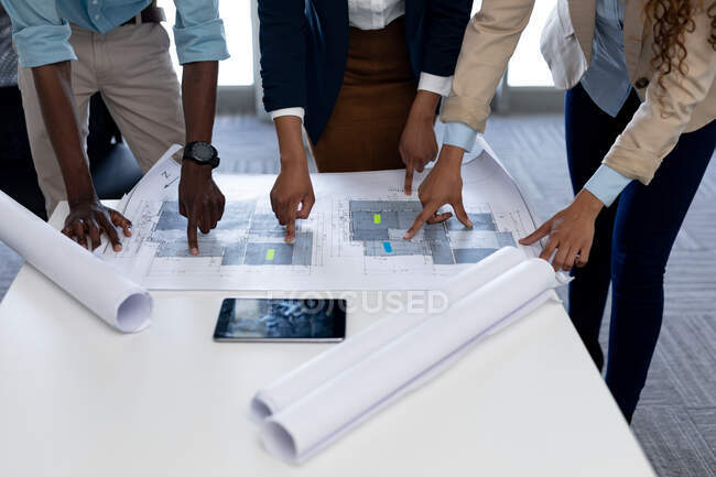 Arquitectos multiraciales masculinos y femeninos señalando el plano durante la reunión en la oficina creativa. negocio, arquitecto y oficina creativa. - foto de stock