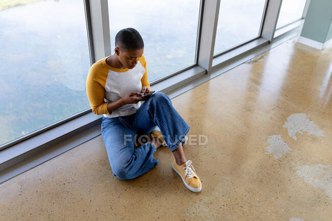 Messagerie texte femme d'affaires créative via smartphone tout en étant assis sur le sol dans le bureau. entreprise indépendante créative, technologie sans fil et bureau. — Photo de stock