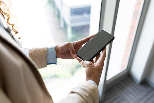 Mittelschicht Geschäftsfrau mit Smartphone mit Kopierraum durch Fenster im Büro. Business, Büroarbeitsplätze und drahtlose Technologie. — Stockfoto